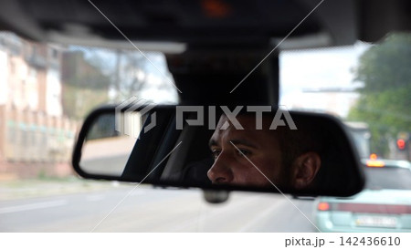 Eyes of male driver reflecting in rearview mirror while riding motor auto. Young man looking concentrated to urban road during operating electric vehicle. Confident guy driving modern car at city Eyes of male driver reflecting in rearview mirror while riding motor auto. Young man looking concentrated to urban road during operating electric vehicle. Confident guy driving modern car at city 142436610