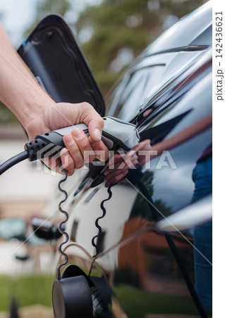 Man holding power supply cable at electric vehicle charging station. Man holding power supply cable at electric vehicle charging station. 142436621