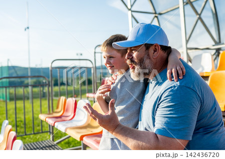 Father and son cheering for football team during match at stadium. 142436720