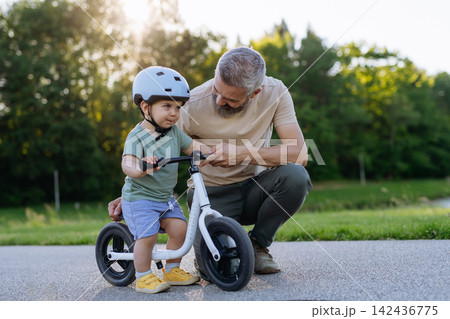 Father teaching toddler son to ride balance bike while wearing safety helmet. Father teaching toddler son to ride balance bike while wearing safety helmet. 142436775
