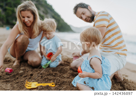 Two toddler children playing on sand beach with paretns during summer holiday. Two toddler children playing on sand beach with paretns during summer holiday. 142436897