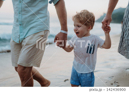 Parents holding hands with little toddler girl, walking on beach during beach holiday. Parents holding hands with little toddler girl, walking on beach during beach holiday. 142436900