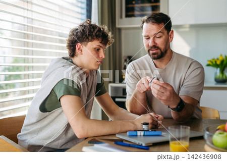 Father checking blood sugar level of diabetic teenage son using glucose meter. Father checking blood sugar level of diabetic teenage son using glucose meter. 142436908