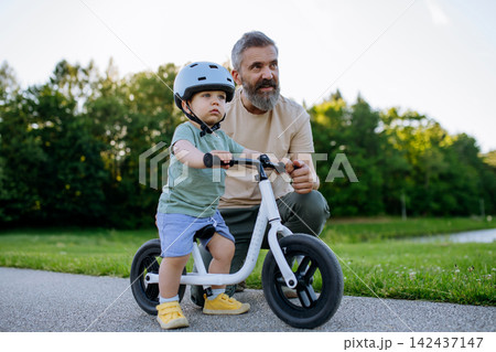 Father teaching toddler son to ride balance bike while wearing safety helmet. Father teaching toddler son to ride balance bike while wearing safety helmet. 142437147