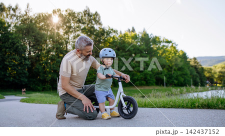 Father teaching toddler son to ride balance bike while wearing safety helmet. Father teaching toddler son to ride balance bike while wearing safety helmet. 142437152