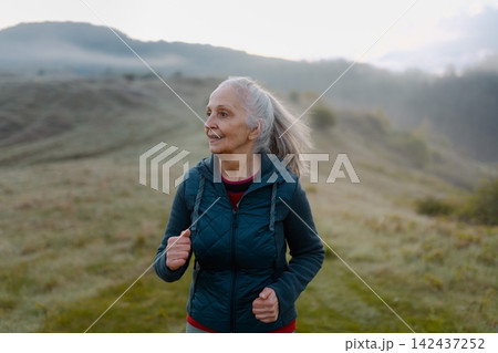 Senior woman jogging in nature on early morning with fog and mountains in background. 142437252