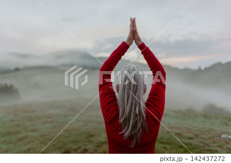 Senior woman meditating outdoors in peaceful mountain landscape at sunrise. 142437272