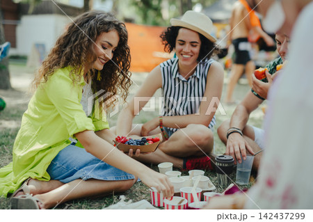Group of young friends at summer festival, sitting on the ground and eating. Group of young friends at summer festival, sitting on the ground and eating. 142437299