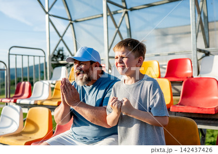 Father and son cheering for football team during match at stadium. Father and son cheering for football team during match at stadium. 142437426