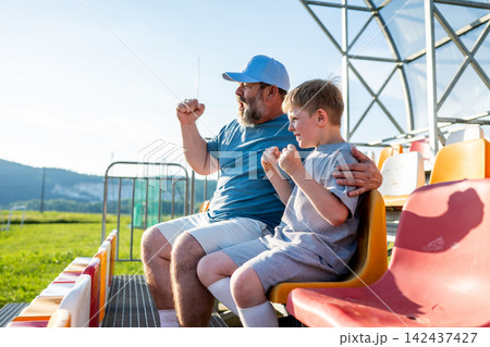 Father and son cheering for football team during match at stadium. Father and son cheering for football team during match at stadium. 142437427