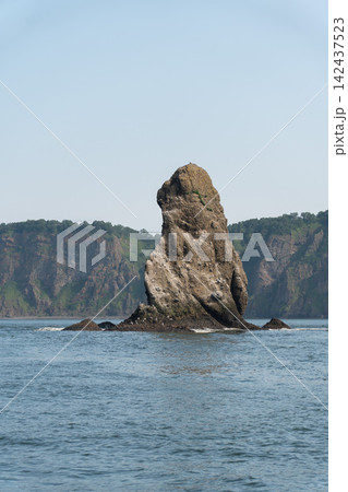 Isolated Three Brothers sea stack stands in Pacific Ocean against green cliffs of Kamchatka coast. Geology, natural landmark, solitude, exploration, tourism. Isolated Three Brothers sea stack stands in Pacific Ocean against green cliffs of Kamchatka coast. Geology, natural landmark, solitude, exploration, tourism. 142437523