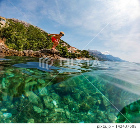 Young boy jumping from coastal rocks into Adriatic Sea on family holiday. Young boy jumping from coastal rocks into Adriatic Sea on family holiday. 142437688