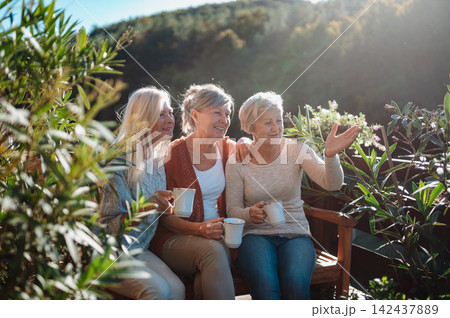 Senior female friends enjoying coffee together on cabin terrace getaway. 142437889
