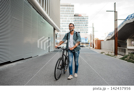 Man pushing his bike by his side, walking down the street. Man pushing his bike by his side, walking down the street. 142437956