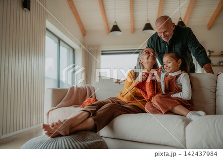 Little girl sitting on sofa with her grandparents and learning to knit indoors at home. Little girl sitting on sofa with her grandparents and learning to knit indoors at home. 142437984