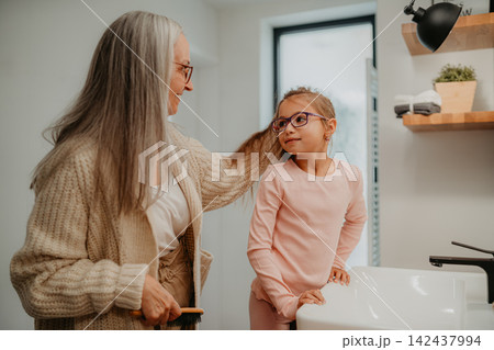 Grandmother making a ponytail to her granddaughter in bathroom in the morning. Grandmother making a ponytail to her granddaughter in bathroom in the morning. 142437994