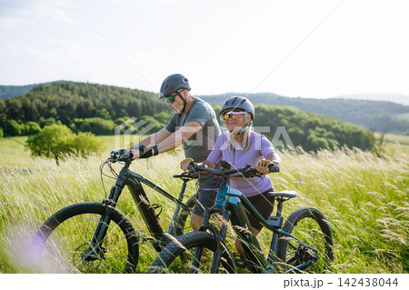 Senior couple taking break during e-bike ride, enjoying nature around them. 142438044
