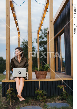 Young woman sitting on tiny house patio, working on laptop. Young woman sitting on tiny house patio, working on laptop. 142438085
