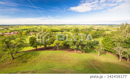 Panoramic rural landscape with rolling green hills, lush trees, distant village, and bright blue sky on a clear day. Region of Bavaria in Germany, Europe. 142438177