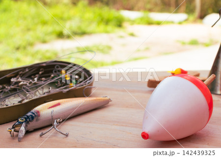 Fishing gear spread out on a wooden surface, including a colorful lure, a sinker, a float and a box of hooks, preparing for a relaxing day of fishing. High quality photo. Fishing gear spread out on a wooden surface, including a colorful lure, a sinker, a float and a box of hooks, preparing for a relaxing day of fishing. High quality photo. 142439325