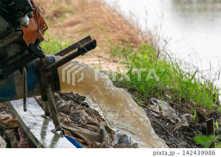 Water pump discharging strong stream into rural canal beside green grass showing irrigation drainage agricultural water management 142439986