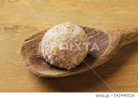 Brazilian coconut beijinho on a wooden spoon on a rustic wooden table. Traditional confectionery for parties and celebrations. Brazilian coconut beijinho on a wooden spoon on a rustic wooden table. Traditional confectionery for parties and celebrations. 142440526