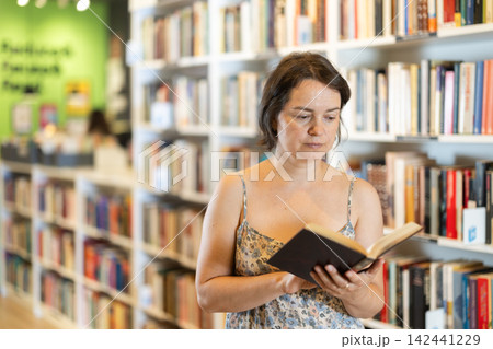 Middle-aged woman choosing books in large bookstore Middle-aged woman choosing books in large bookstore 142441229