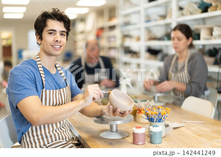 Young man applying coating with brush on ceramic piece Young man applying coating with brush on ceramic piece 142441249