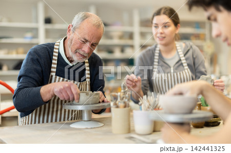 Mature man at table molds cup from wet clay in pottery workshop Mature man at table molds cup from wet clay in pottery workshop 142441325