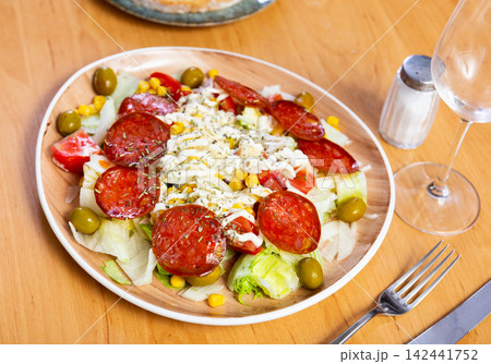 Delicious salad with following ingredients: pork sausage, avocado, corn, salt, olives, tomato, onion 142441752