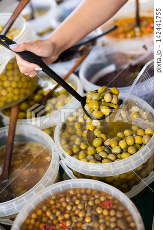 Hand holds spoon with a portion of pickled olives, onions and cucumbers over plastic container. Fresh green olives at farmers market Hand holds spoon with a portion of pickled olives, onions and cucumbers over plastic container. Fresh green olives at farmers market 142441755
