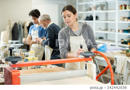 Girl in pottery workshop works with machine clay press roller Girl in pottery workshop works with machine clay press roller 142442036