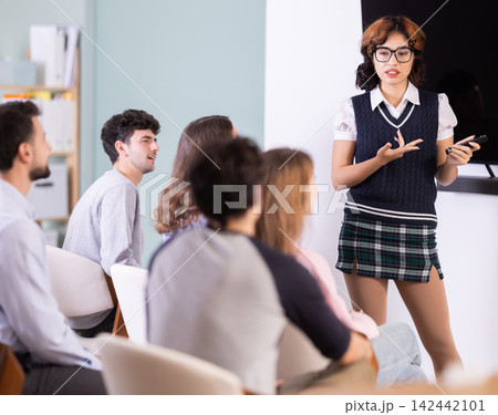Female lecturer communicates with students, controls projector using remote control. 142442101