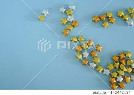 Glitter gold and silver origami lucky stars scattered on pastel blue background Glitter gold and silver origami lucky stars scattered on pastel blue background 142442154