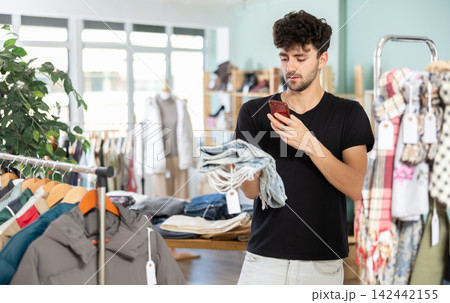 Young guy scanning QR-code on jeans pantaloons in clothing store Young guy scanning QR-code on jeans pantaloons in clothing store 142442155