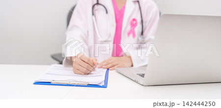 Professional doctor wearing lab coat using laptop and taking report notes on notebook for Breast Cancer Awareness month, World Cancer Day, National Cancer Survivors Month and Pink October in hospital 142444250