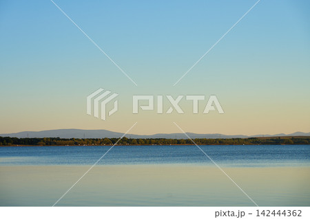Calm lake with distant hills under clear evening sky Calm lake with distant hills under clear evening sky 142444362