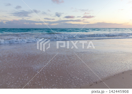 Calm ocean waves roll onto a wide sandy beach at sunset, leaving delicate foam Calm ocean waves roll onto a wide sandy beach at sunset, leaving delicate foam 142445908