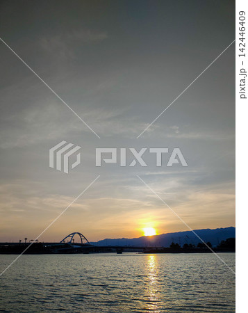 山並みに沈む夕日と水面に反射する美しいサンセット、アーチ橋を望むウォーターフロントの風景 142446409