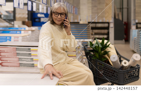 Woman shopping for home improvement materials, talking on phone in a building supply store Woman shopping for home improvement materials, talking on phone in a building supply store 142448157