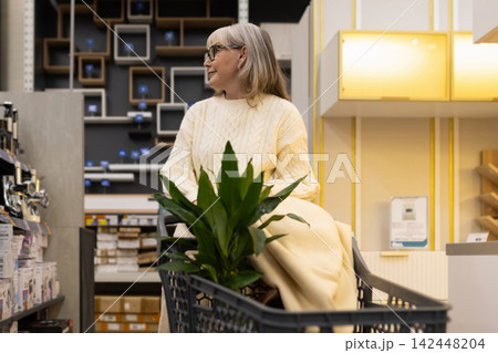 Woman pushing a shopping cart with a plant in a retail store aisle 142448204