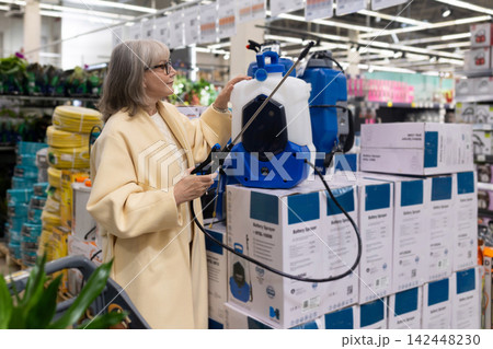 Senior woman shopping for a battery sprayer in a home improvement store Senior woman shopping for a battery sprayer in a home improvement store 142448230