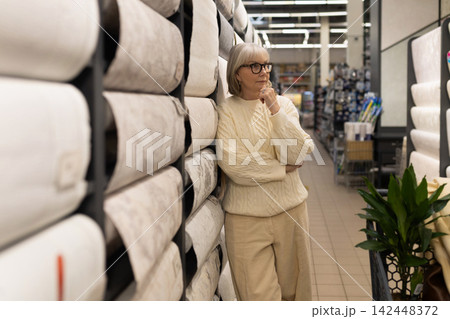 Mature woman leaning on wallpaper rolls, thoughtfully deciding on home decor Mature woman leaning on wallpaper rolls, thoughtfully deciding on home decor 142448372