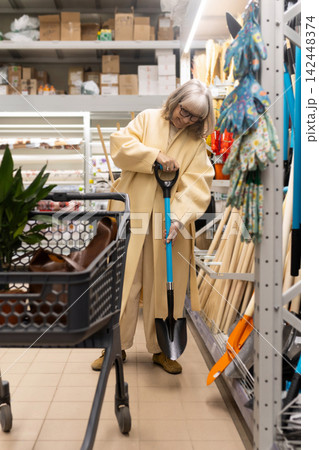 Senior woman holding a shovel while shopping for gardening supplies in a retail store 142448374