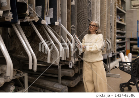 Mature woman looking at rugs and carpets in a warehouse store Mature woman looking at rugs and carpets in a warehouse store 142448396