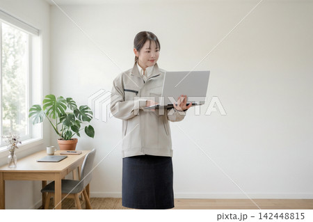 立ったままノートパソコンを確認する女性 立ったままノートパソコンを確認する女性 142448815