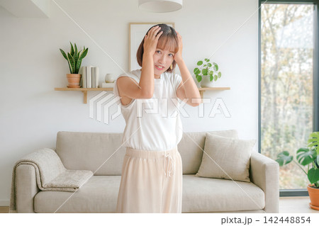 リビングで頭を抱える困った表情の女性 リビングで頭を抱える困った表情の女性 142448854