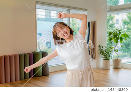 ヨガスタジオで両手を上げて元気に踊る笑顔の女性 ヨガスタジオで両手を上げて元気に踊る笑顔の女性 142448860