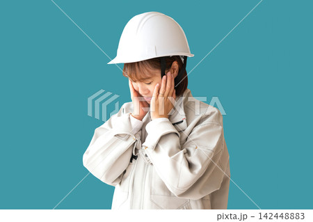 青緑の背景で耳をふさぐヘルメット姿の作業服の女性 青緑の背景で耳をふさぐヘルメット姿の作業服の女性 142448883