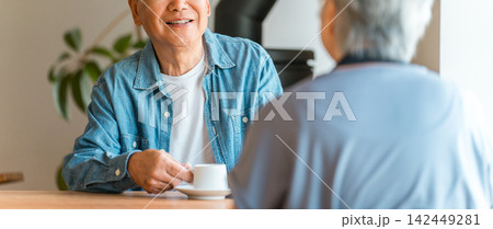自宅のダイニングテーブルでコーヒーを飲みながら笑顔で会話するシニア夫婦 自宅のダイニングテーブルでコーヒーを飲みながら笑顔で会話するシニア夫婦 142449281